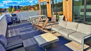 Una terraza en la azotea con mobiliario exterior, incluyendo un sofá, sillas y una mesa de centro.