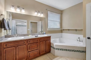 A bathroom with two sinks, a large bathtub, wooden cabinets, a mirror, and a window with blinds. - Midtown Home, Pets Welcome! (Tallahassee)
