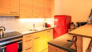 Une cuisine avec des meubles de rangement en bois, un réfrigérateur rouge, un évier et une cuisinière.
