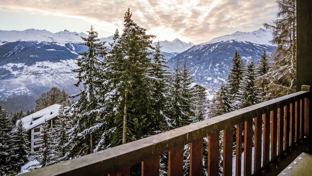 Un chalet de montagne doté d’un balcon en bois offrant une vue sur un paysage enneigé et des montagnes.