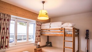 Une chambre avec un lit superposé, une fenêtre, une lampe et un aspirateur.