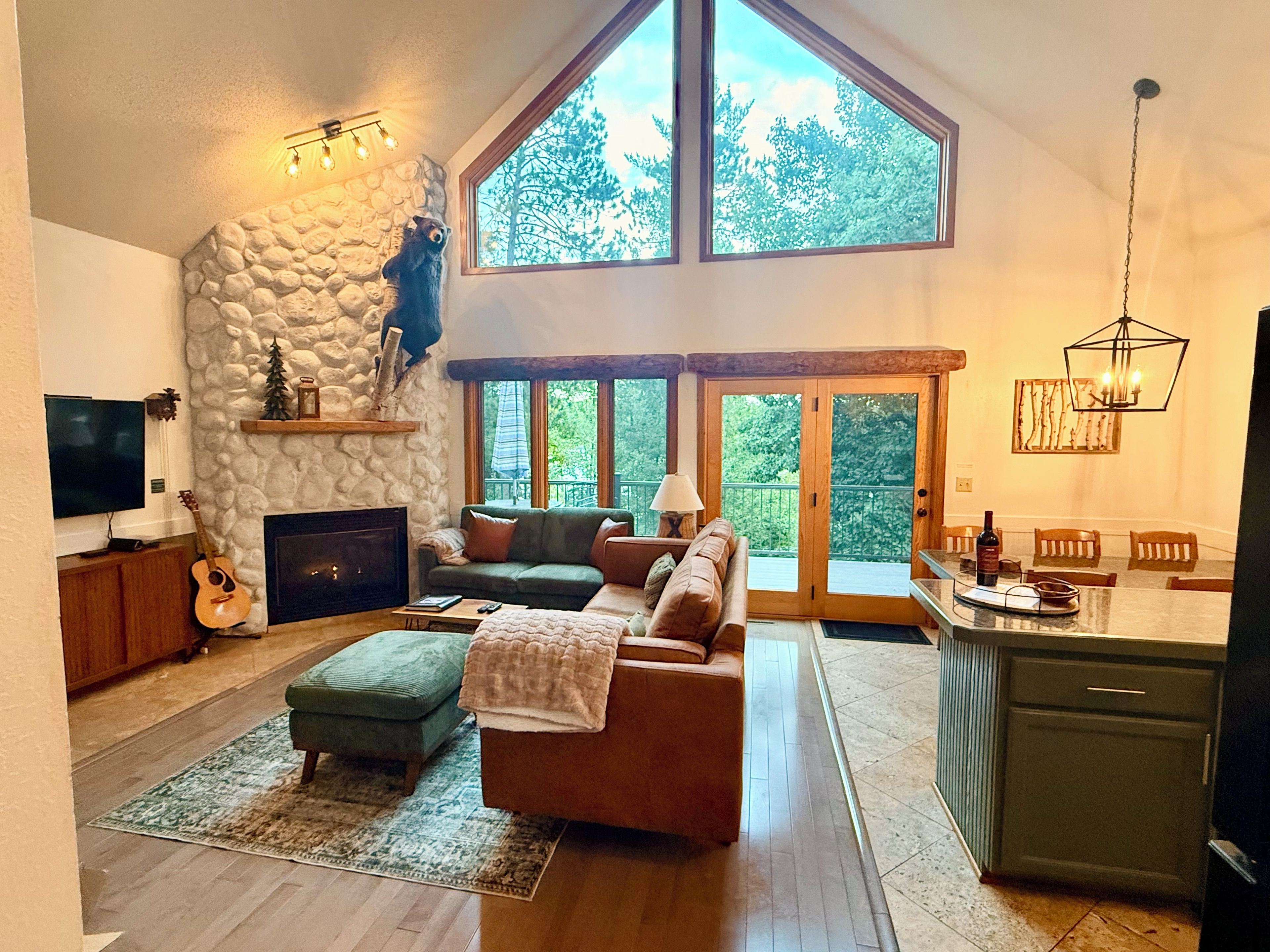 A spacious living room with a stone wall, a fireplace, a large window, and a dining area with a chandelier.