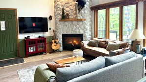A cozy living room with a stone fireplace, a mounted bear, a television, and a guitar.