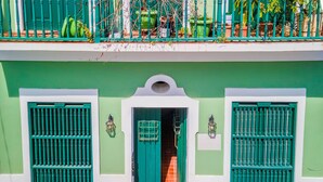 A building with a green facade, two large windows with green shutters, and a small entrance with a tiled floor.