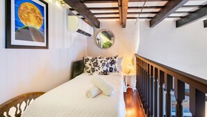 A bedroom with a bed, a round mirror, a framed picture, and a view of the city through the window.