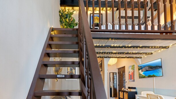 A staircase with a wooden railing leading to a second floor. There is a desk with a chair, a television mounted on the wall, and a plant on the landing.