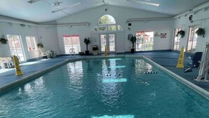 Ein Innenpool mit klarem Wasser, umgeben von blauem Boden, sowie Sicherheitszeichen und einem Rettungsschwimmerstuhl.