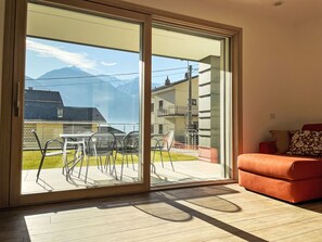 A room with a sliding glass door leading to an outdoor patio with a table and chairs, a red sofa, and a view of mountains.