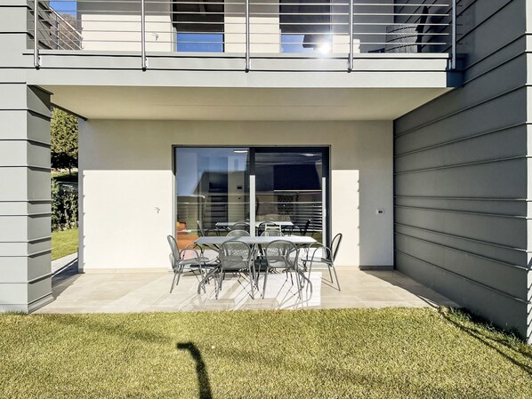 A modern outdoor patio with a dining table and chairs, a glass door entrance, and a view of the surrounding area.