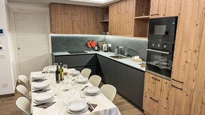 A modern kitchen with wooden cabinets, a built-in oven, and a dining area set for six with white chairs and a table.