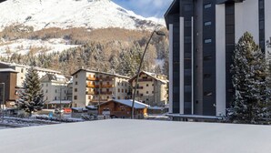 Een modern hotel met uitzicht op een piste, dat traditionele en moderne architectuur combineert, met een imposante berg op de achtergrond.