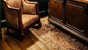 Una habitación con una silla de madera, un armario de madera y cuadros en la pared.