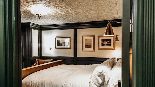 Una habitación de hotel con una cama grande, un banco de madera, un candelabro y cuadros en la pared.