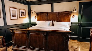 Una cama grande de madera oscura con sábanas blancas, con dos lámparas fijadas a la pared.