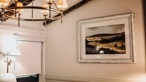 A hallway with a chandelier, a framed landscape painting, and a door with a light fixture. - The Donna King Suite - Bootleggers Lodge on Lake Nokomis (Tomahawk)
