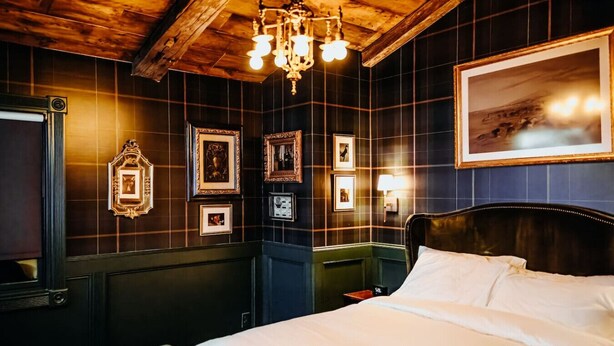 Una habitación con techo de madera, una cama con sábanas blancas y cuadros en las paredes.