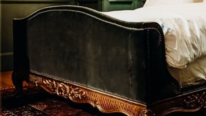 Una habitación con una cama de cabecera de madera oscura, una mesita de noche verde y un tapete estampado.