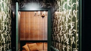 Un pasillo estrecho con suelo de madera, paredes verdes con diseños blancos y un sofá de cuero marrón en el centro.