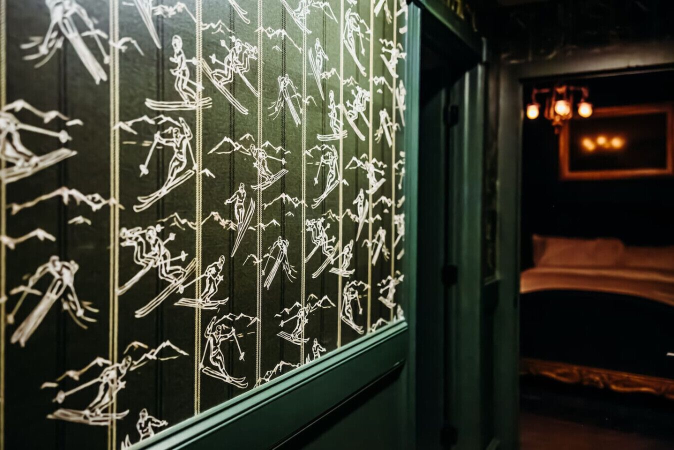 A room with a bed, a window with white line drawings of people in various activities, and a chandelier.
