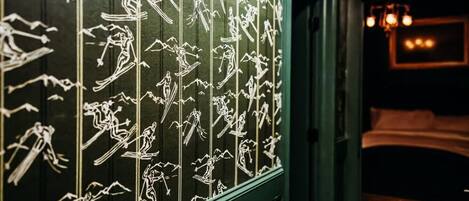 A room with a bed, a window with white line drawings of people in various activities, and a chandelier.
