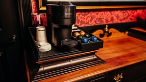 Una cafetera con un dispensador para cápsulas Nespresso, una taza de café y una bandeja con cápsulas de café de colores sobre una superficie de madera.