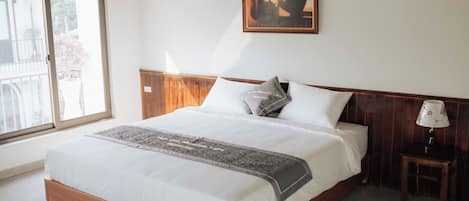A neatly made bed with a wooden headboard, a bedside table with a lamp, and a window with a view of the outside.