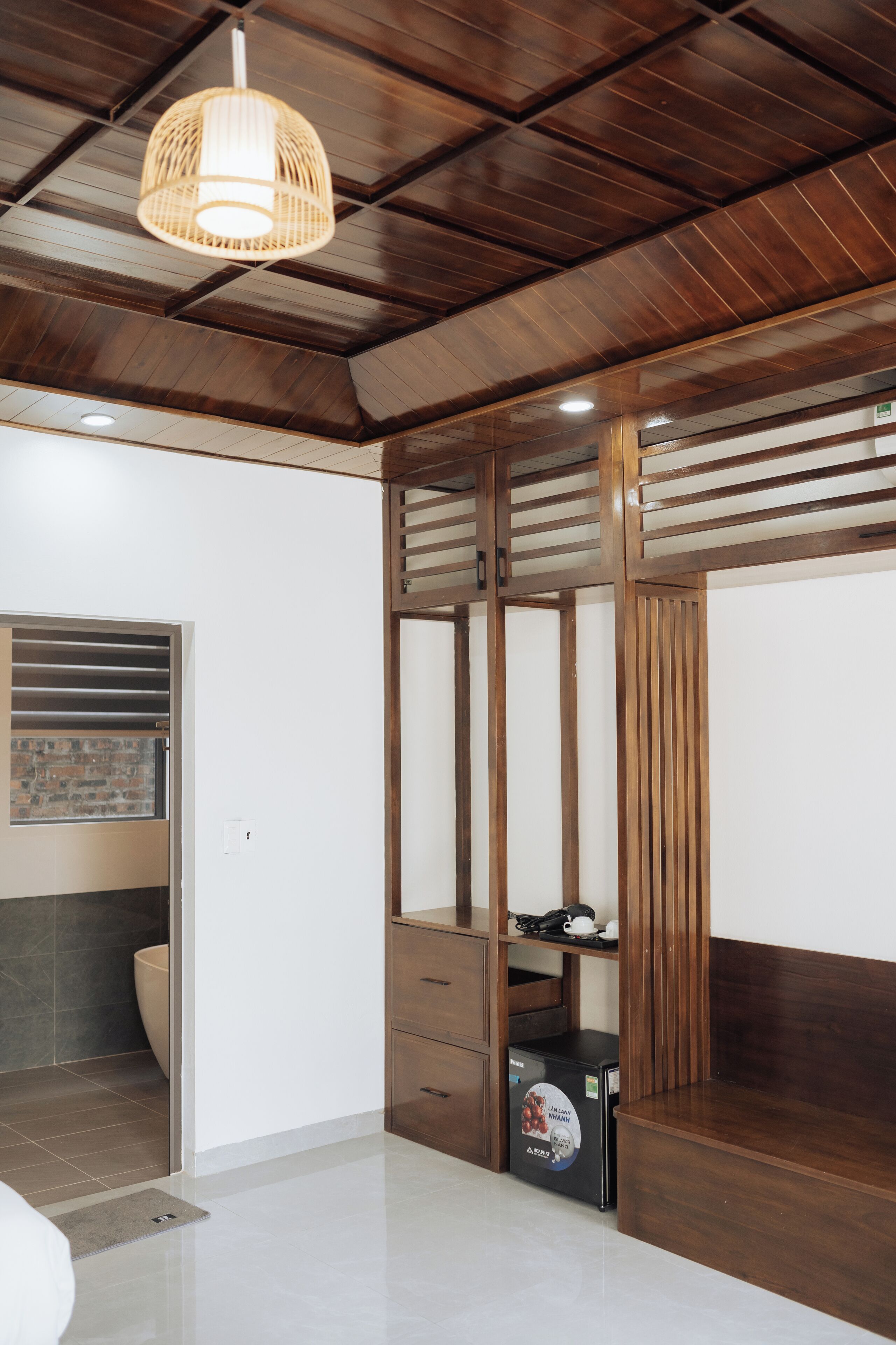 Un baño moderno con techo de madera, una lámpara colgante, un inodoro y un mueble pequeño.