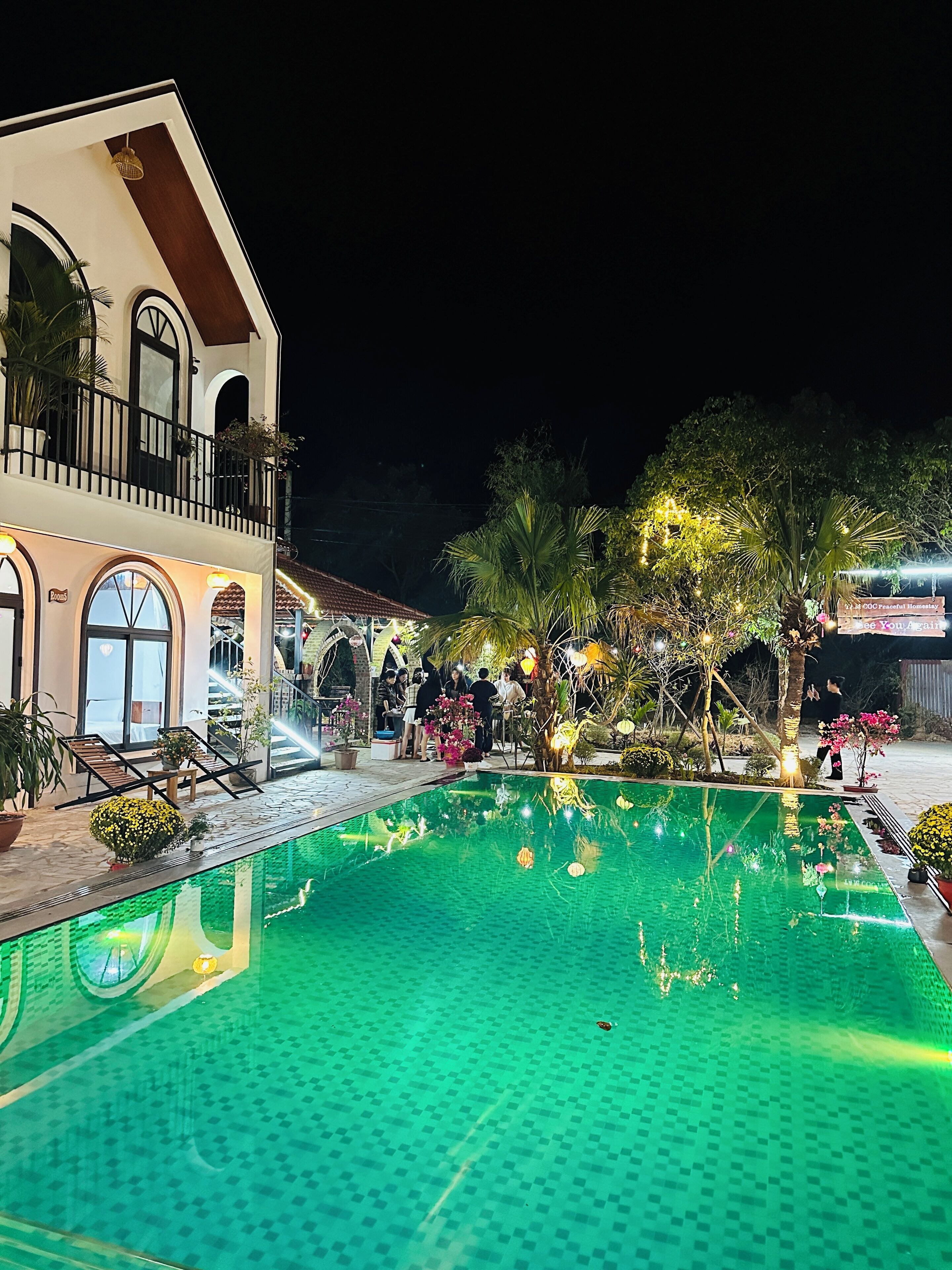 A pool area with a tiled floor, a building with a balcony, and potted plants.