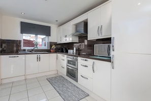 A modern kitchen with white cabinets, stainless steel appliances, and a window with a view. - House - Sleeps 10 - Parking - WiFi (Barrow-in-Furness)