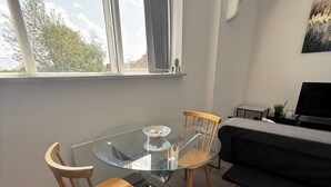 A modern living room with a glass dining table, wooden chairs, a black sofa, and a TV. - 1 Bed Flat - Sleeps 2 - Pets - Parking - Wifi (Kettering)