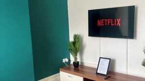 A living room with teal walls, a flat-screen TV mounted on the wall, a wooden coffee table, and a small potted plant on a wooden side table.