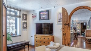 A bedroom with a large bed, a wooden dresser, a bench, a TV, and a door leading to another room.