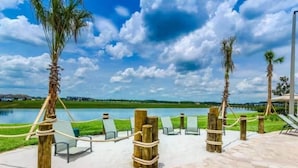 Zona junto a la piscina con sillones de descanso, postes de madera y vistas a un lago.