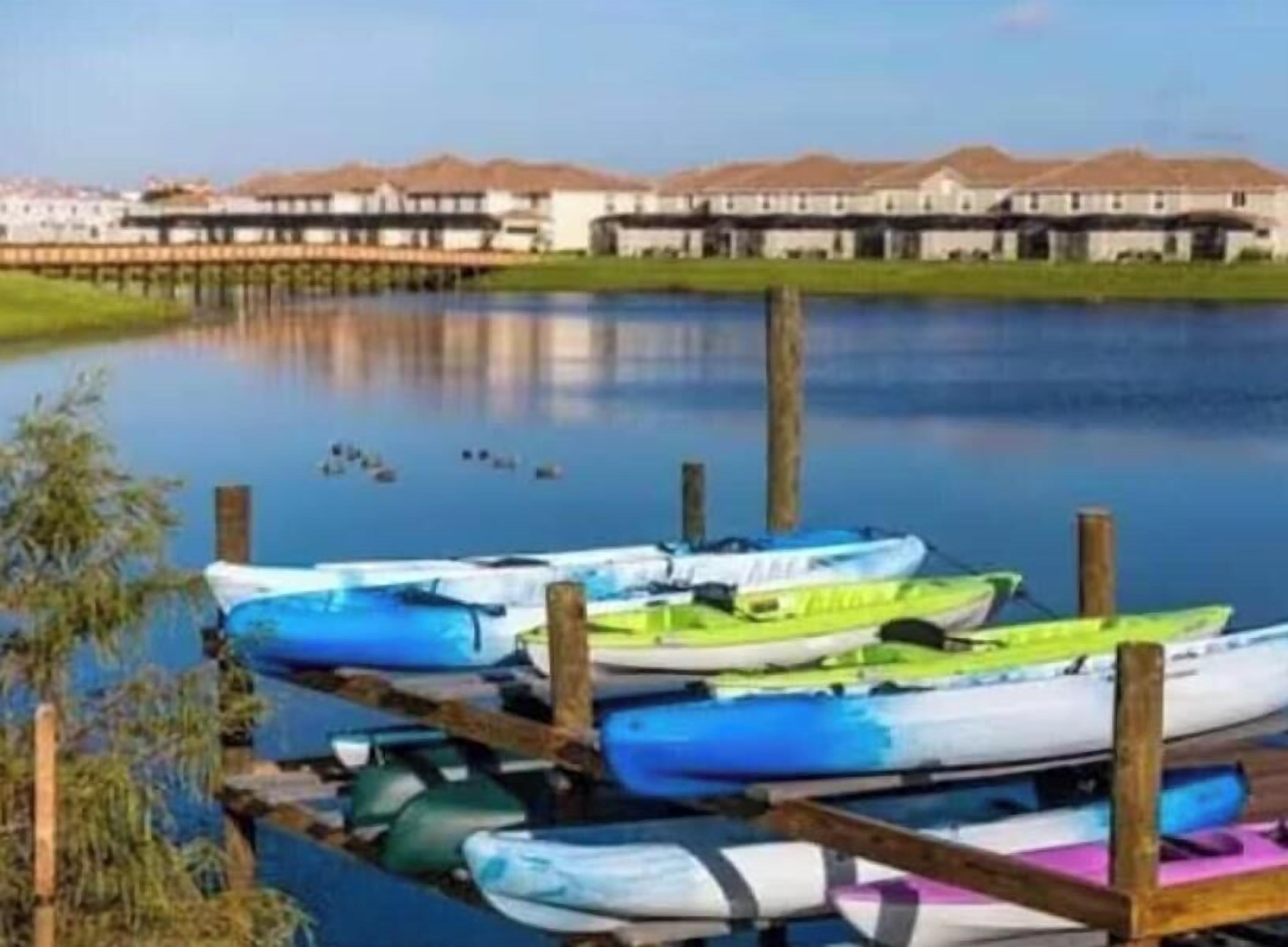 A calm lake with boats docked at a wooden pier, a building with a flat roof in the background.