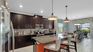 Una cocina moderna con armarios oscuros, encimera de granito y una isla central con taburetes de bar.