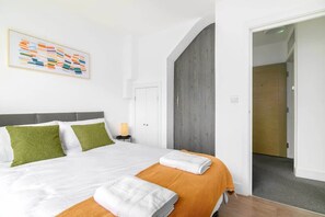 Habitación de hotel con una cama, almohadas verdes, una colcha naranja, una obra de arte enmarcada y una puerta de madera.