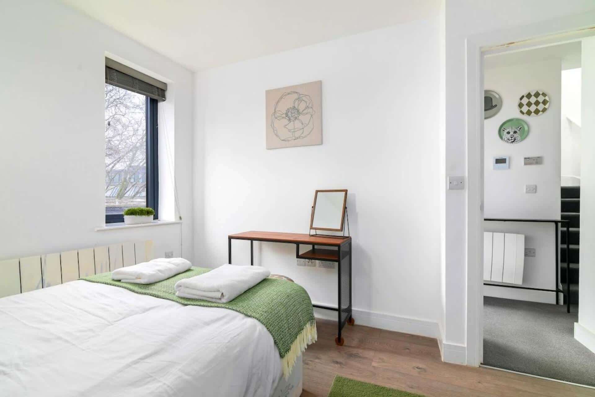 A bedroom with a bed, a window, a desk, and a door leading to a bathroom.