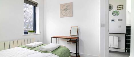 Une chambre à coucher comprenant un lit, une fenêtre, un bureau et une porte donnant sur une salle de bain.
