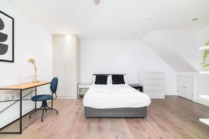 Un dormitorio moderno con cama, escritorio, silla y una mesita de noche.