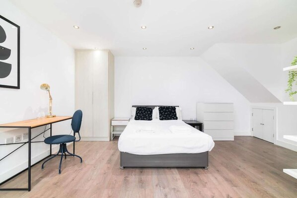 Un dormitorio moderno con cama, escritorio, silla y una mesita de noche.