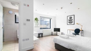 A modern bedroom with a bed, a desk, a chair, a television, and a window with a view.