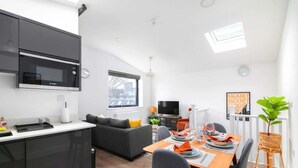 A modern kitchen with a Bosch microwave, a dining area with a table set for two, and a living area with a sofa and a television.