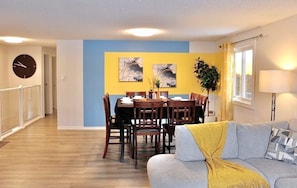 A dining area with a table and chairs, a sofa, a clock, and a plant.