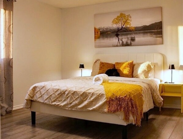 Un dormitorio con cama, un cuadro, una mesita de noche y una lámpara.
