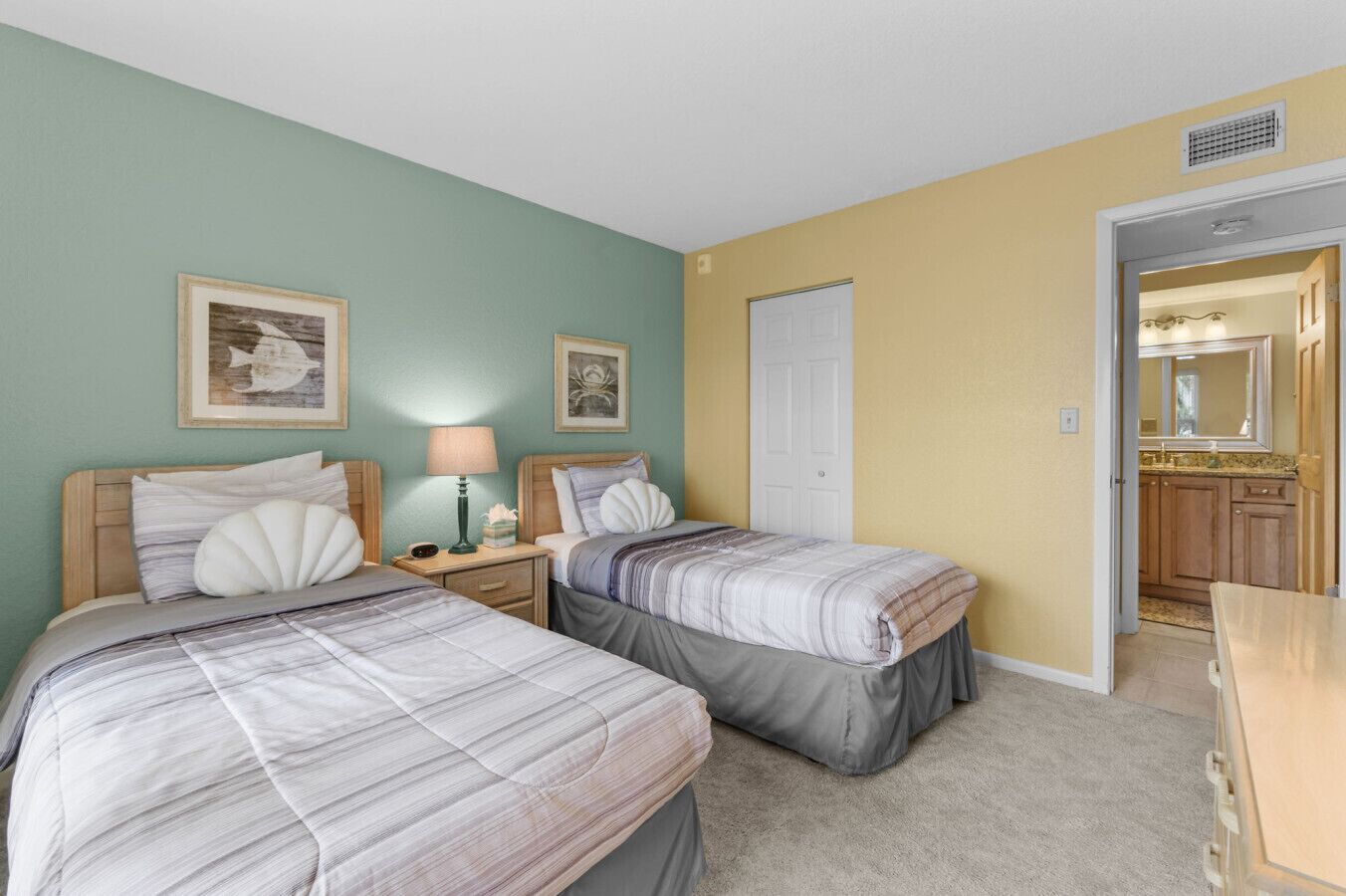 Une chambre avec deux lits, une table de chevet avec une lampe et une porte donnant sur une salle de bain.