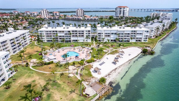 A resort with multiple buildings, a central pool, and a beach area.