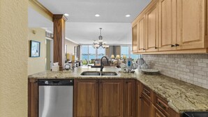 A kitchen with wooden cabinets, granite countertops, a dishwasher, and a view of the ocean.