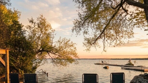 A lakeside view with three lounge chairs, a small table, and a stone wall. - Lake View Loft Studio type (Severn)