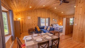 A wooden cabin interior with a dining table set for four, a sofa, a bed, and a ceiling fan. - Lake View Loft Studio type (Severn)