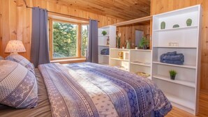 A wooden-paneled bedroom with a bed, a window, and built-in shelving with plants and towels. - Lake View Loft Studio type (Severn)